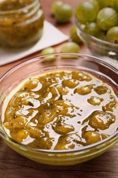 Bowl of delicious gooseberry jam and fresh berries on wooden table, closeup