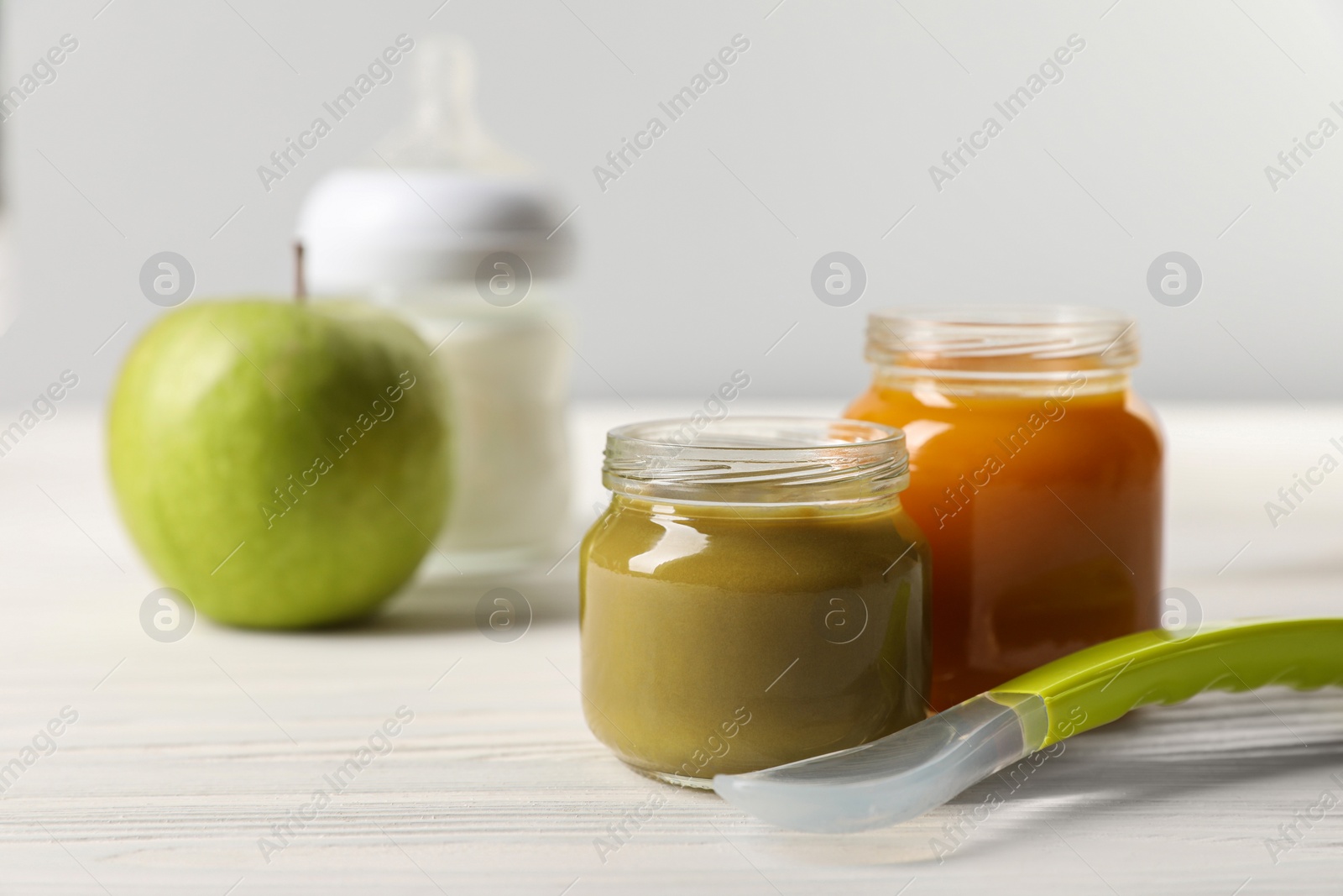 Photo of Jars with healthy baby food and spoon on white wooden table. Space for text