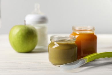 Jars with healthy baby food and spoon on white wooden table. Space for text