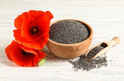 Wooden bowl of poppy seeds, scoop and flowers on white table