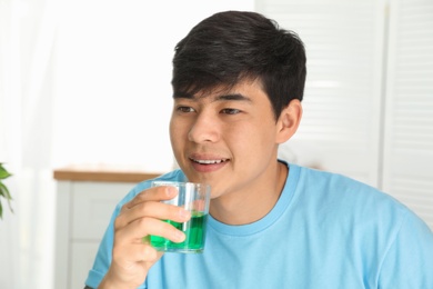 Man holding glass with mouthwash in bathroom. Teeth care