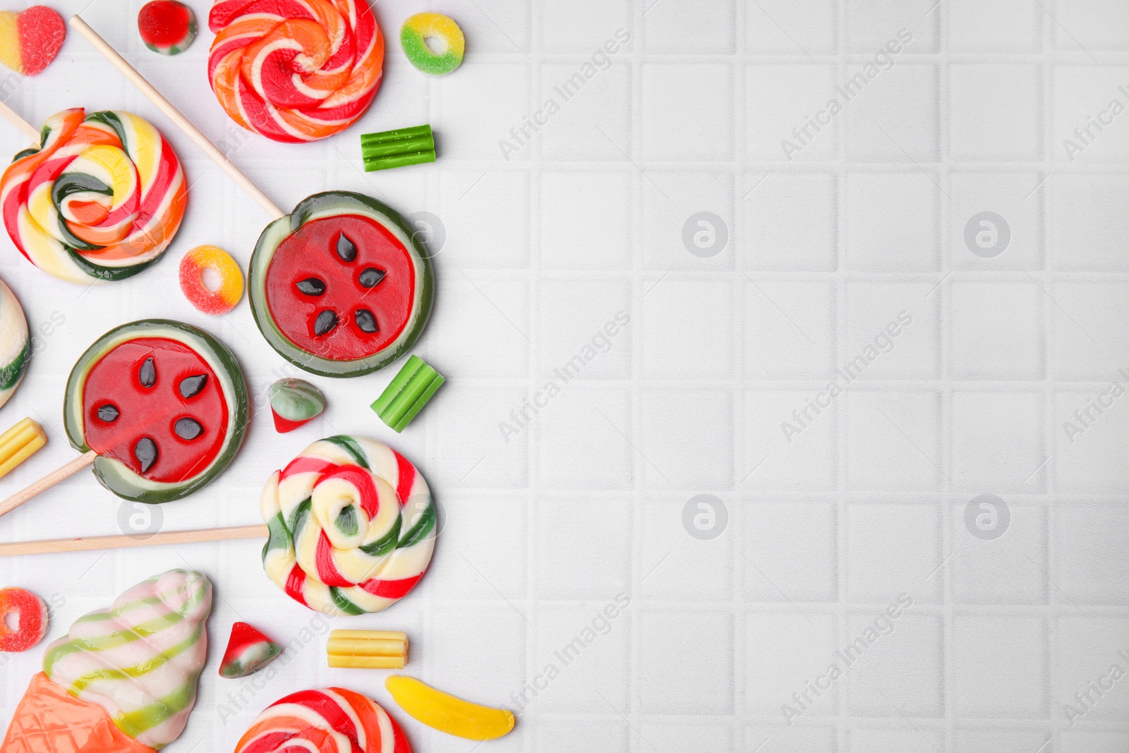 Photo of Many tasty colorful jelly candies and lollipops on white tiled table, flat lay. Space for text