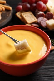 Photo of Dipping piece of bread into tasty cheese fondue at black wooden table, closeup