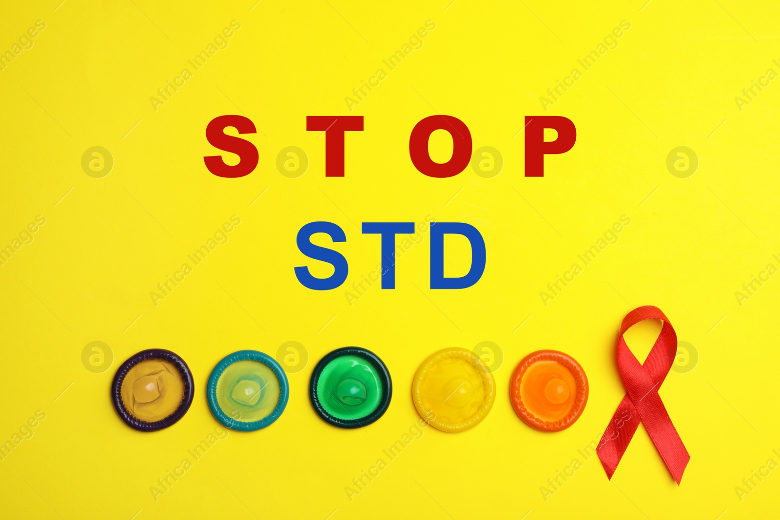 Image of Colorful condoms, red ribbon and text STOP STD on yellow background, flat lay