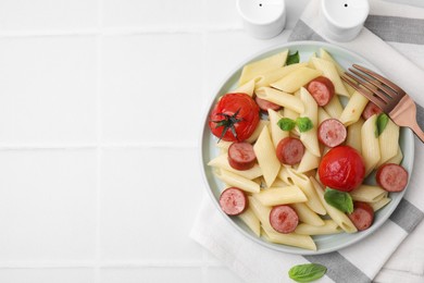 Tasty pasta with smoked sausage, tomatoes and basil served on white tiled table, flat lay. Space for text