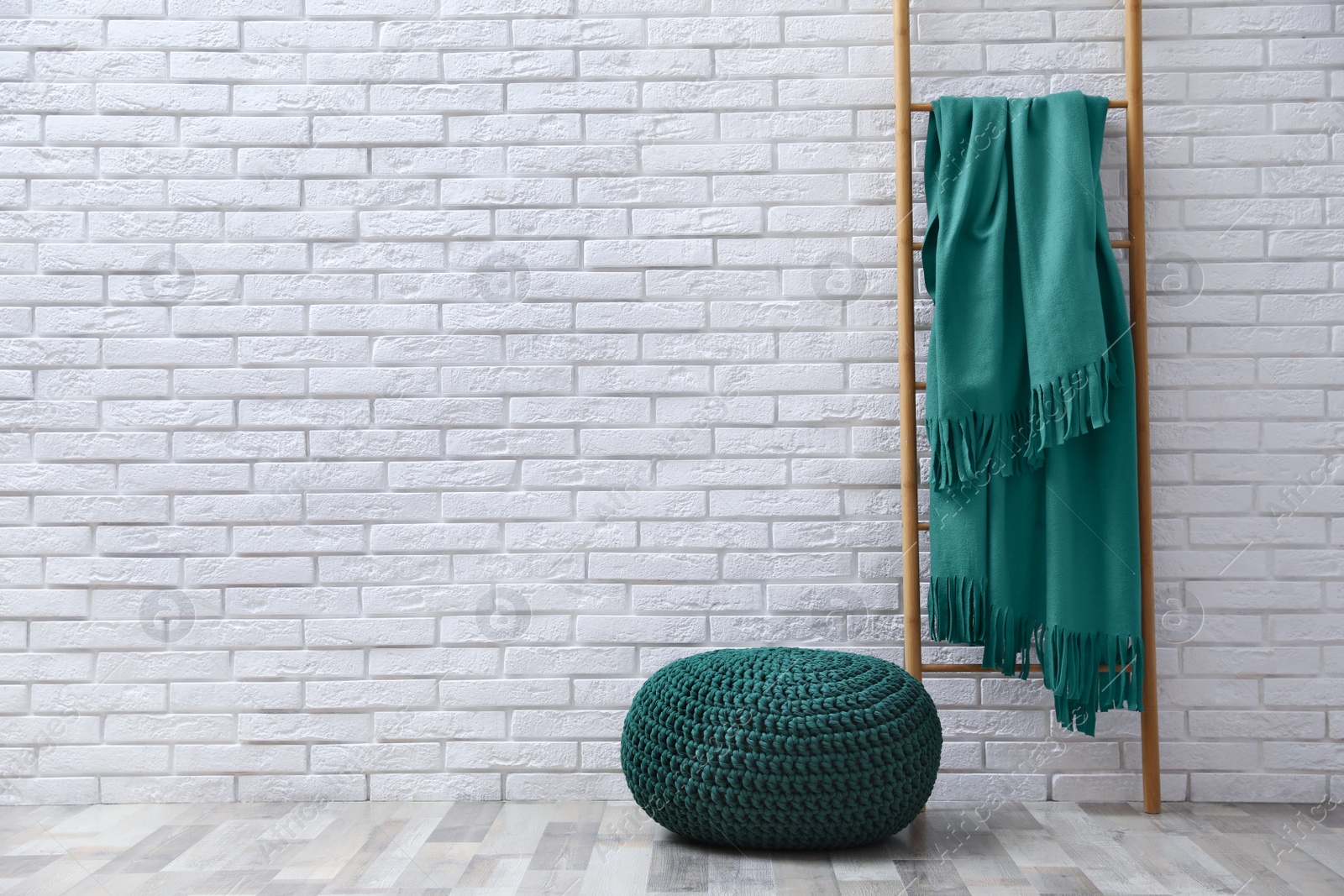 Photo of Stylish knitted pouf and ladder with plaid near white brick wall indoors, space for text. Interior design