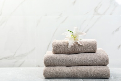 Photo of Stack of fresh towels with flower on grey table against light background. Space for text