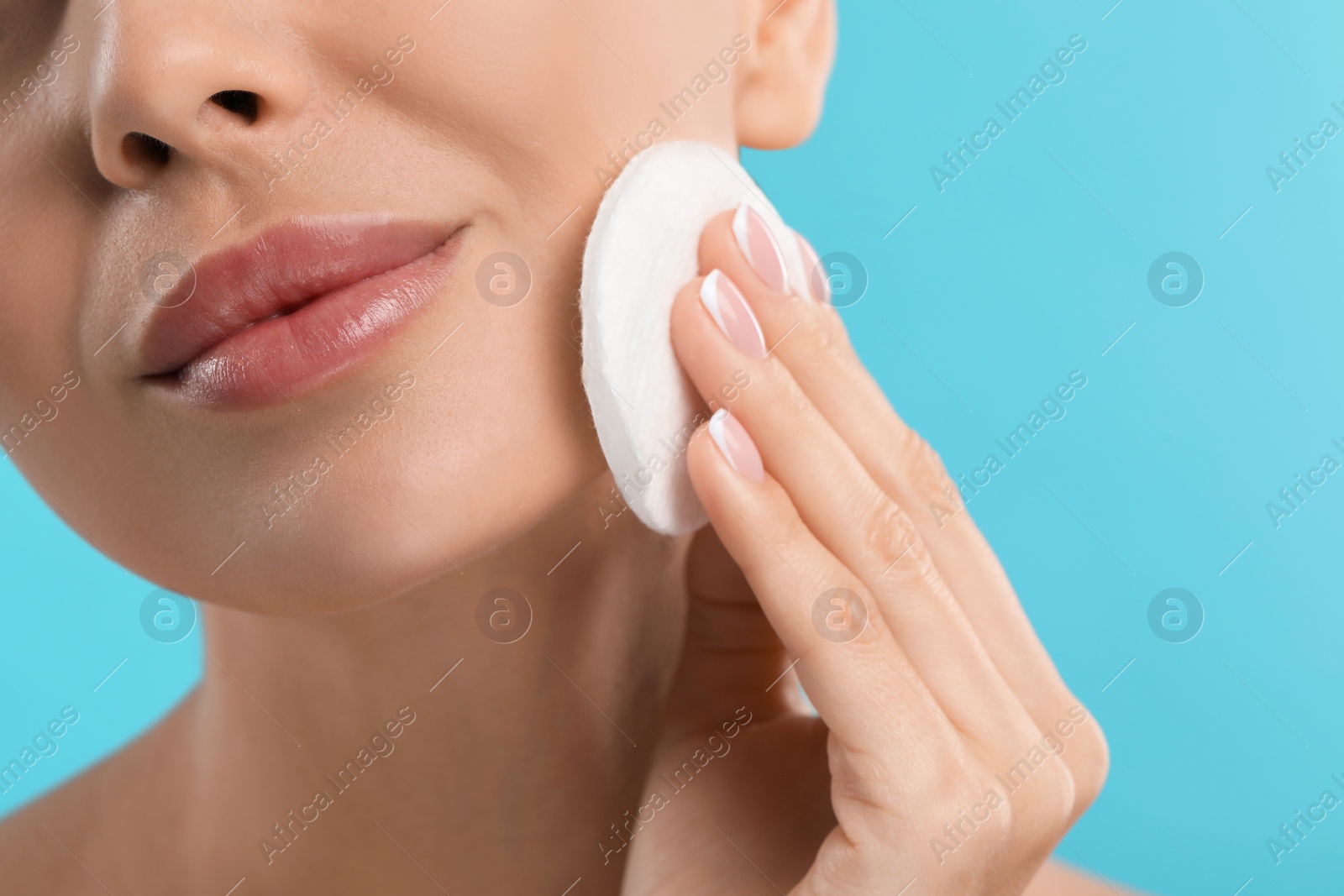 Photo of Beautiful woman removing makeup with cotton pad on light blue background, closeup. Space for text