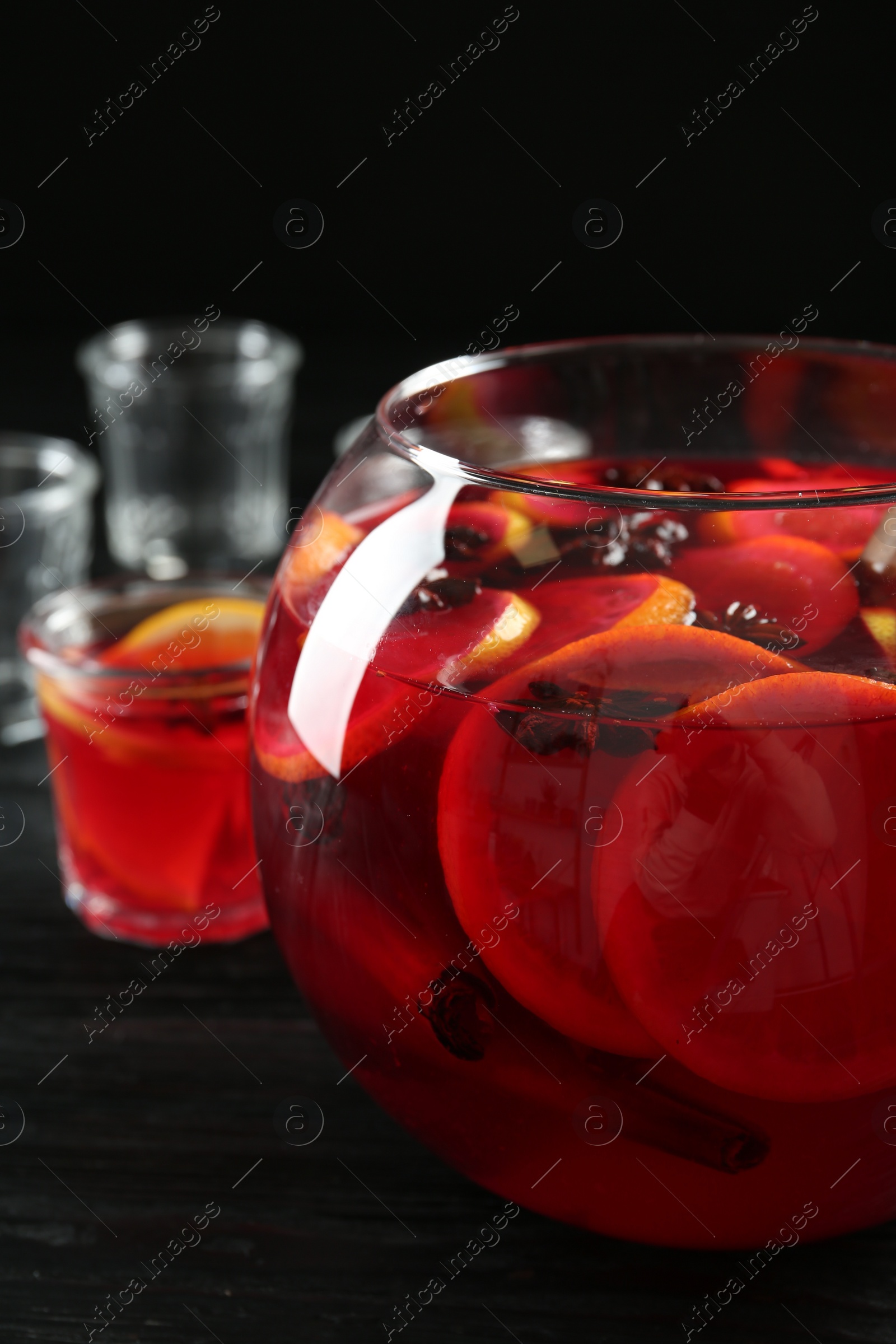 Photo of Glass bowl of delicious aromatic punch drink on black wooden table, closeup