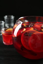 Photo of Glass bowl of delicious aromatic punch drink on black wooden table, closeup