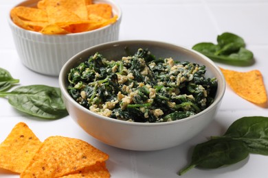 Photo of Tasty spinach dip with egg in bowl and nachos chips on white table, closeup