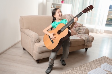 Emotional little girl playing guitar in room