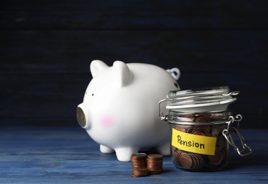 Photo of Piggy bank and jar of coins with word PENSION on table