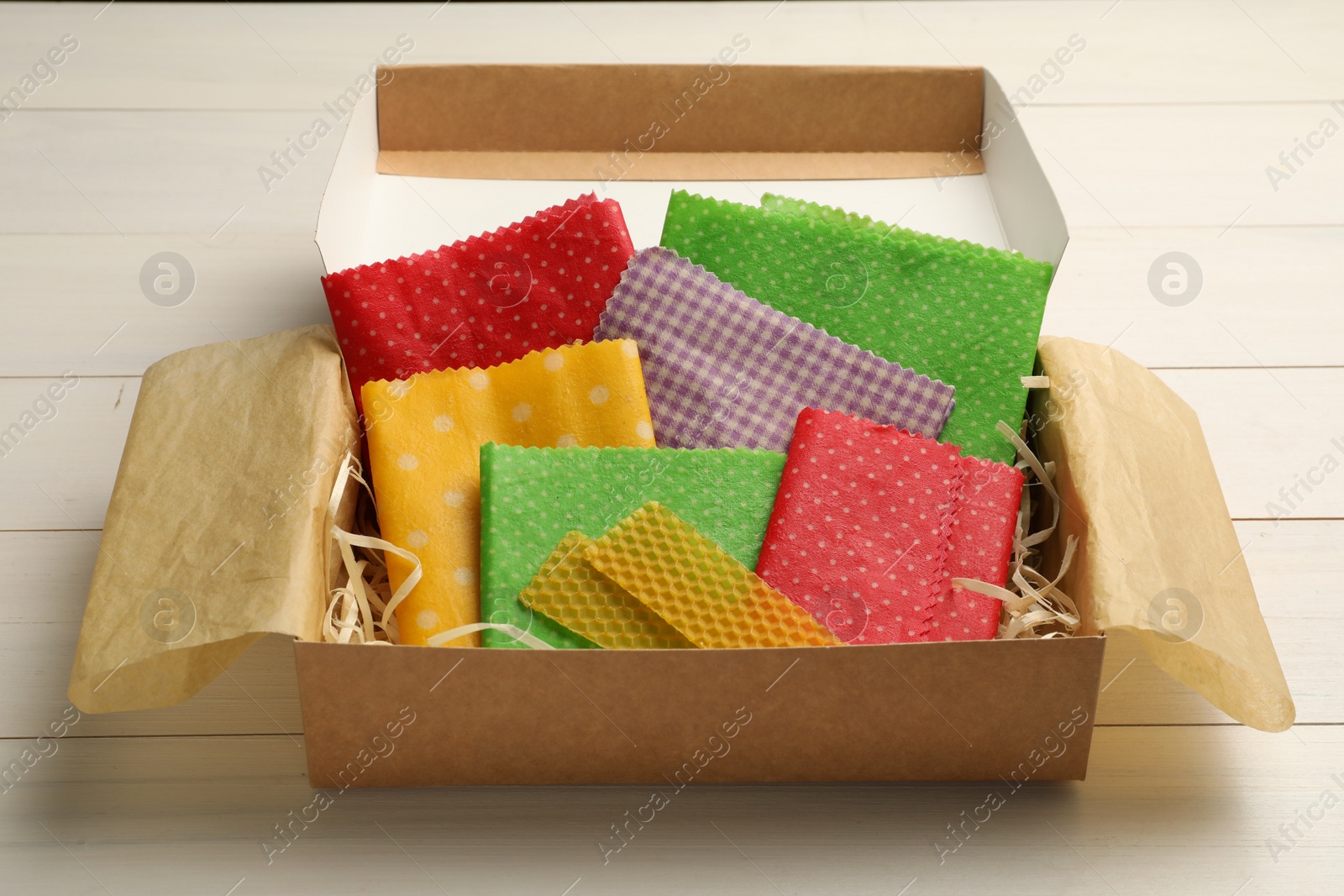 Photo of Colorful beeswax food wraps in box on white wooden table