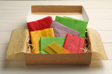 Colorful beeswax food wraps in box on white wooden table