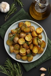 Photo of Delicious baked potatoes with rosemary and ingredients on black table, flat lay