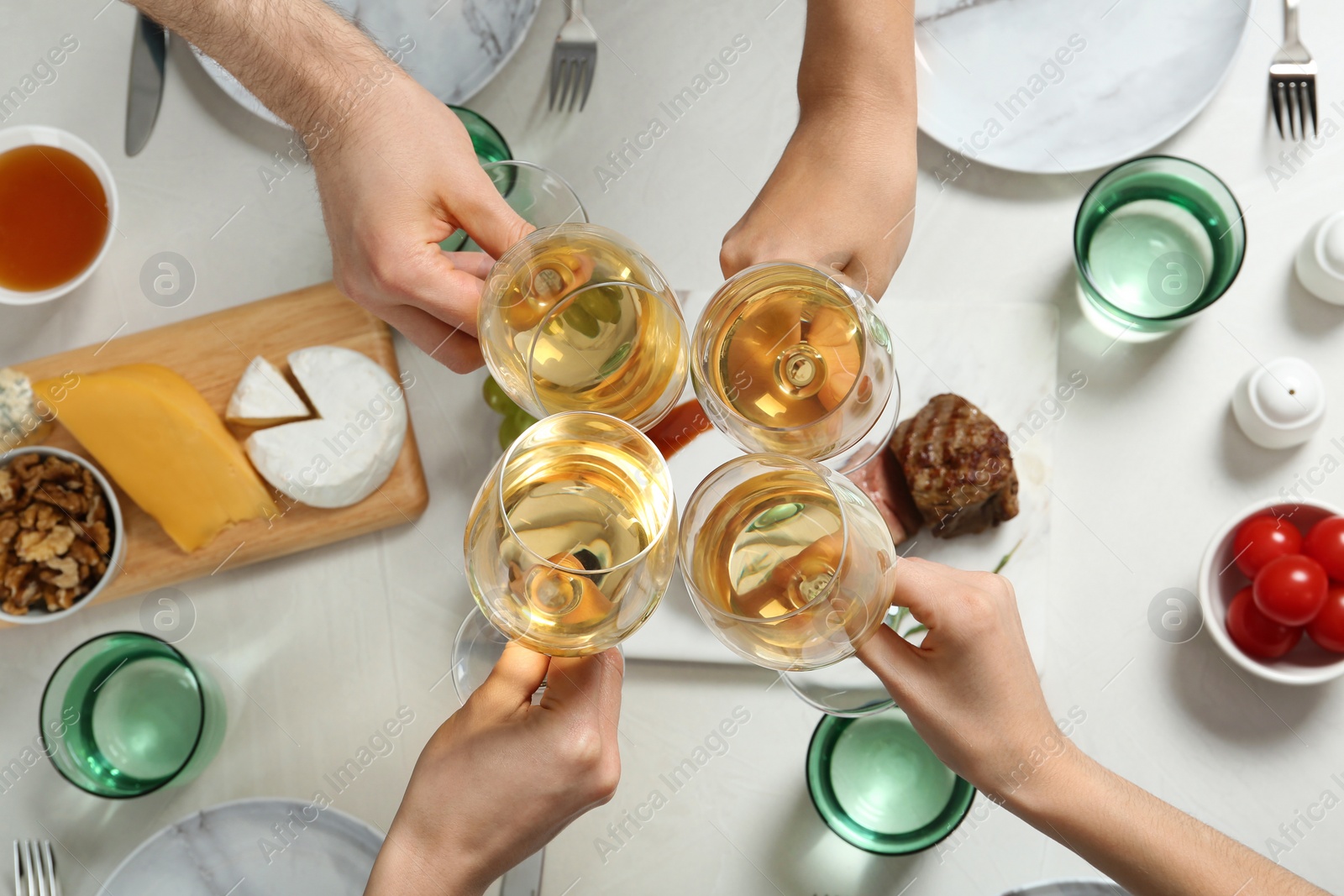 Photo of People holding glasses of white wine over table with tasty snacks, top view