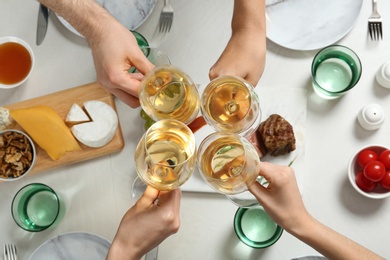 Photo of People holding glasses of white wine over table with tasty snacks, top view