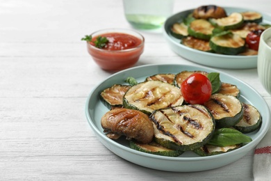 Photo of Delicious grilled zucchini slices served on white wooden table. Space for text