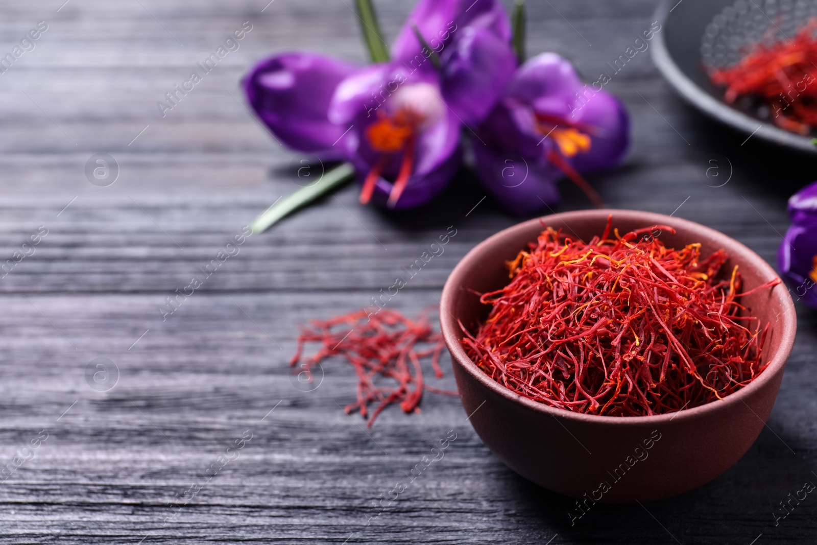 Photo of Dried saffron in bowl and crocus flowers on black wooden table, space for text