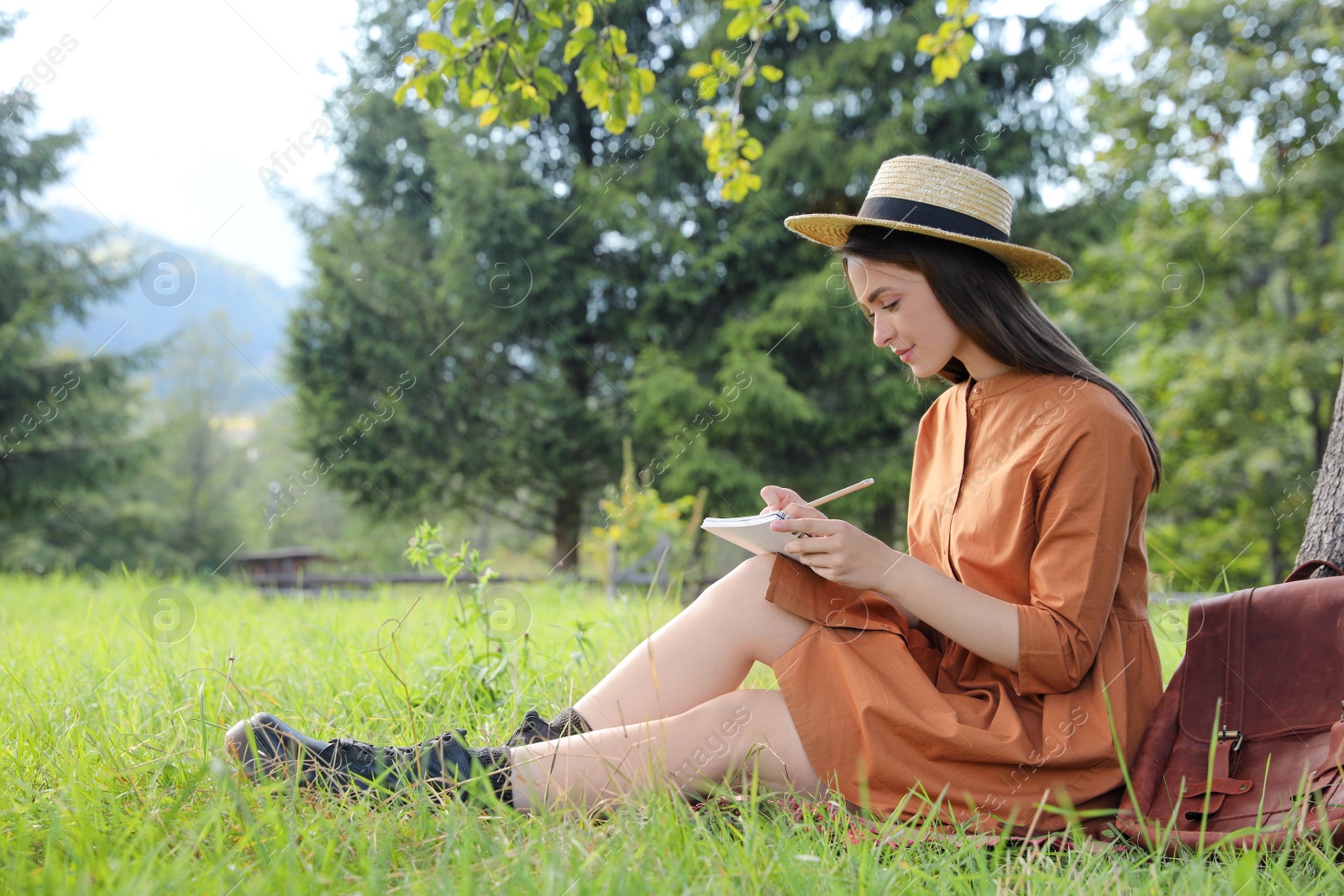 Photo of Beautiful young woman drawing with pencil in notepad outdoors on green grass