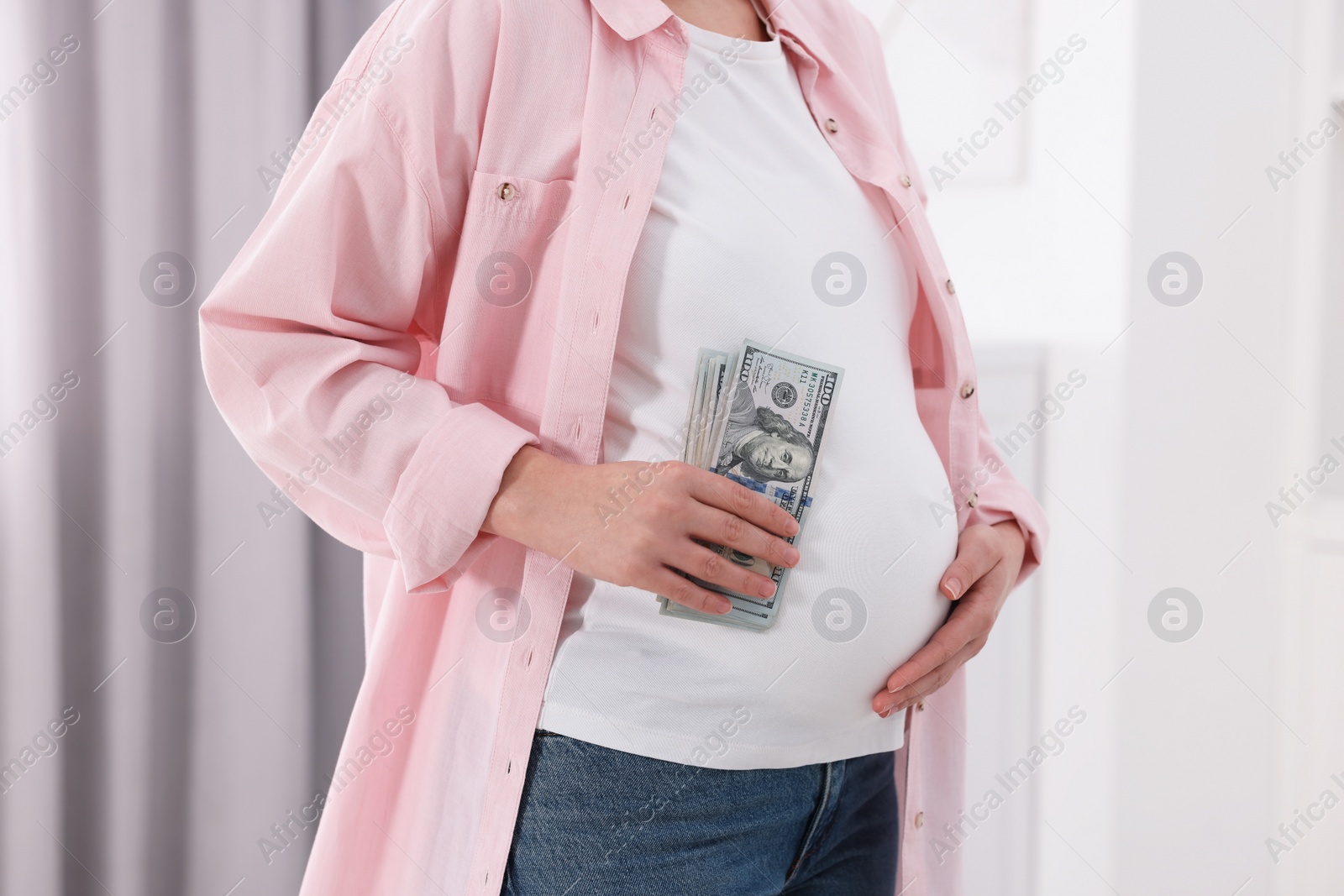 Photo of Surrogate mother. Pregnant woman with dollar banknotes indoors, closeup