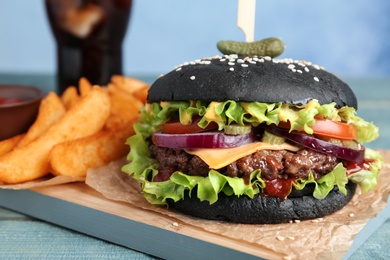 Photo of Board with black burger and french fries on table, closeup