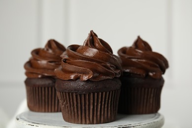 Photo of Delicious chocolate cupcakes with cream on dessert stand against light background, closeup