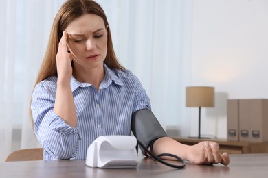 Photo of Woman suffering from headache and measuring blood pressure at wooden table in room, space for text