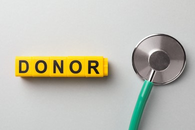 Photo of Word Donor made of cubes and stethoscope on light grey table, flat lay