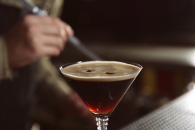 Glass of espresso martini cocktail and blurred bartender on background, closeup