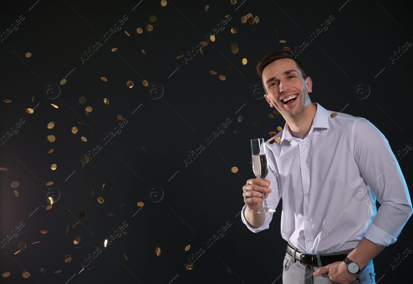 Photo of Handsome man with glass of champagne and confetti on dark background. Space for text