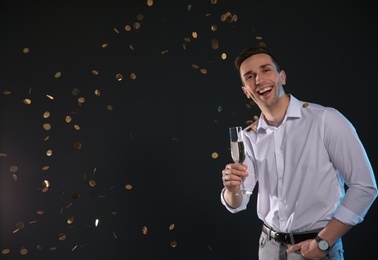 Handsome man with glass of champagne and confetti on dark background. Space for text