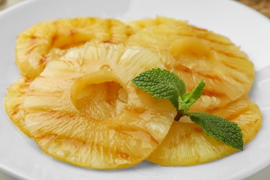 Photo of Tasty grilled pineapple slices and mint on white plate, closeup