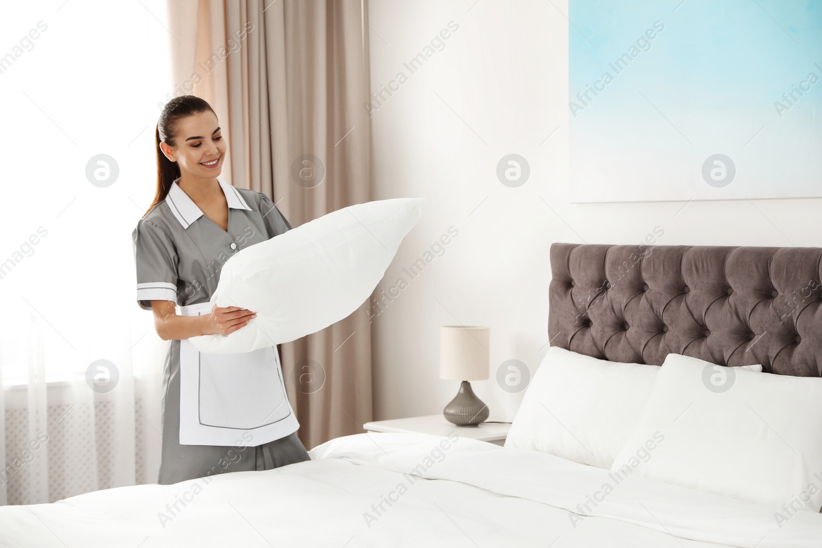 Photo of Young chambermaid making bed in hotel room. Space for text