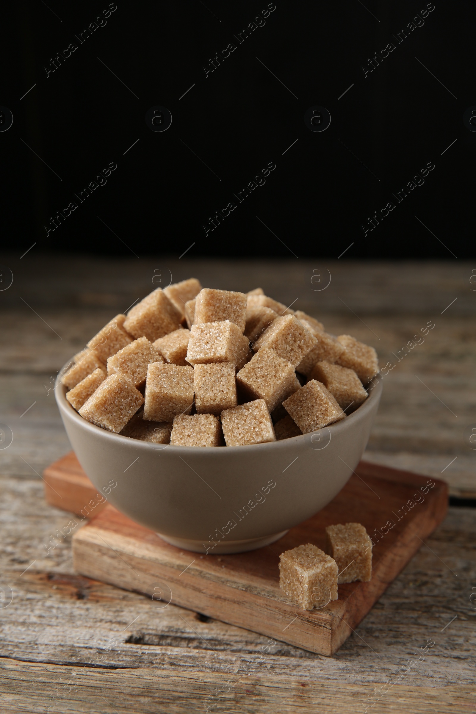 Photo of Brown sugar cubes in bowl on wooden table, closeup