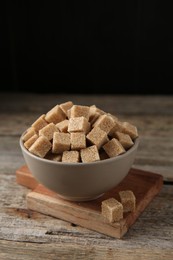 Photo of Brown sugar cubes in bowl on wooden table, closeup