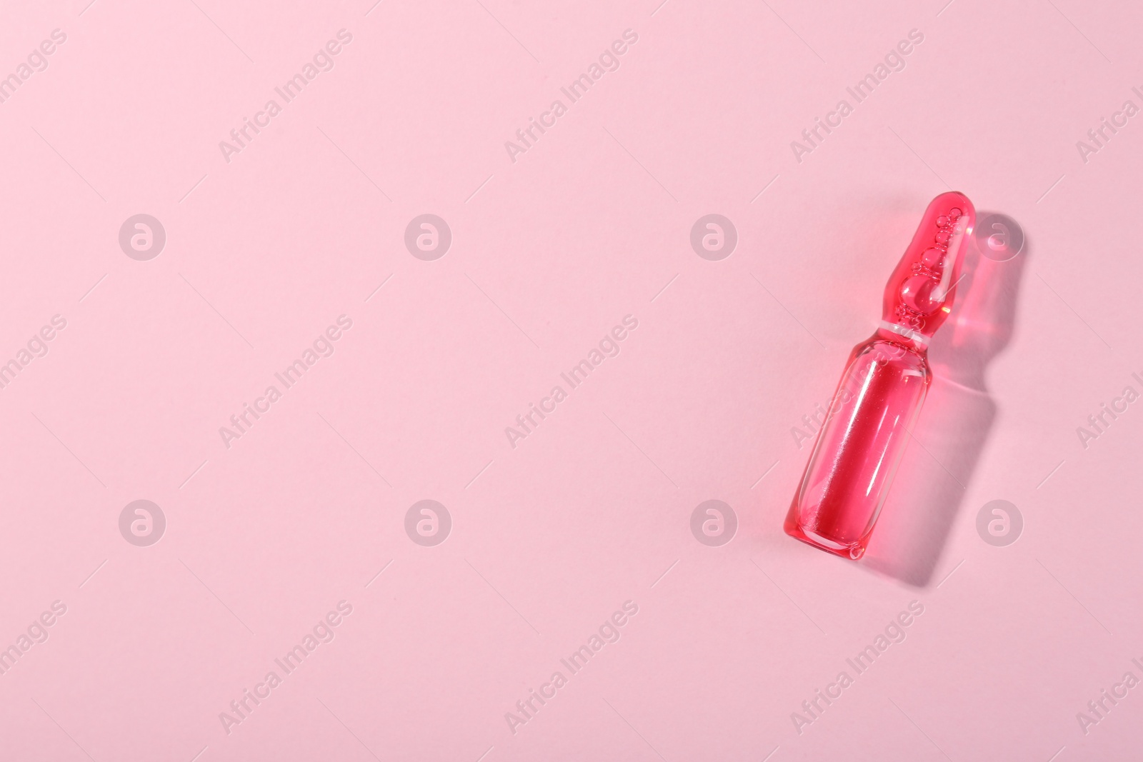 Photo of Glass ampoule with liquid on pink background, top view. Space for text