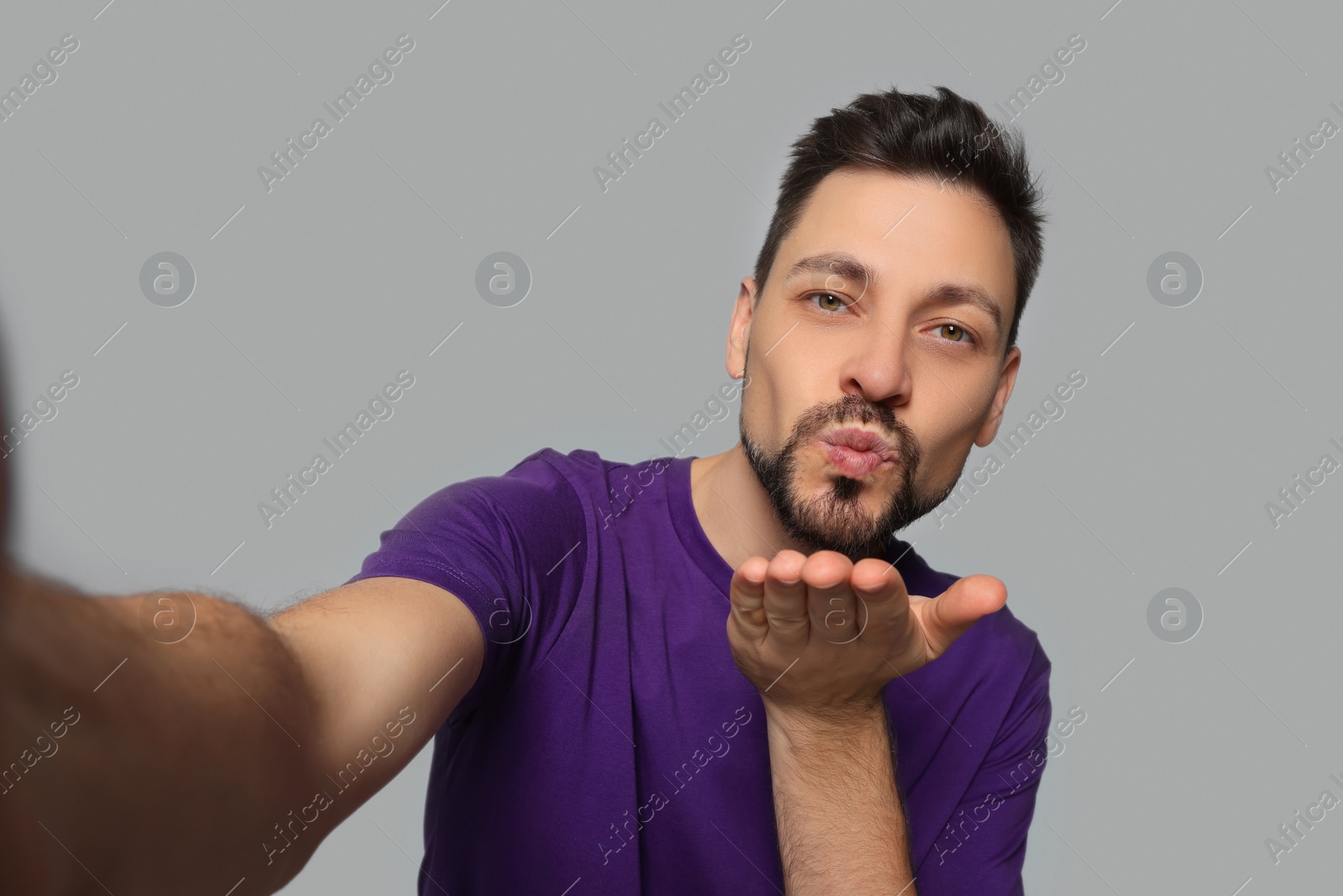 Photo of Handsome man blowing kiss while taking selfie on light grey background