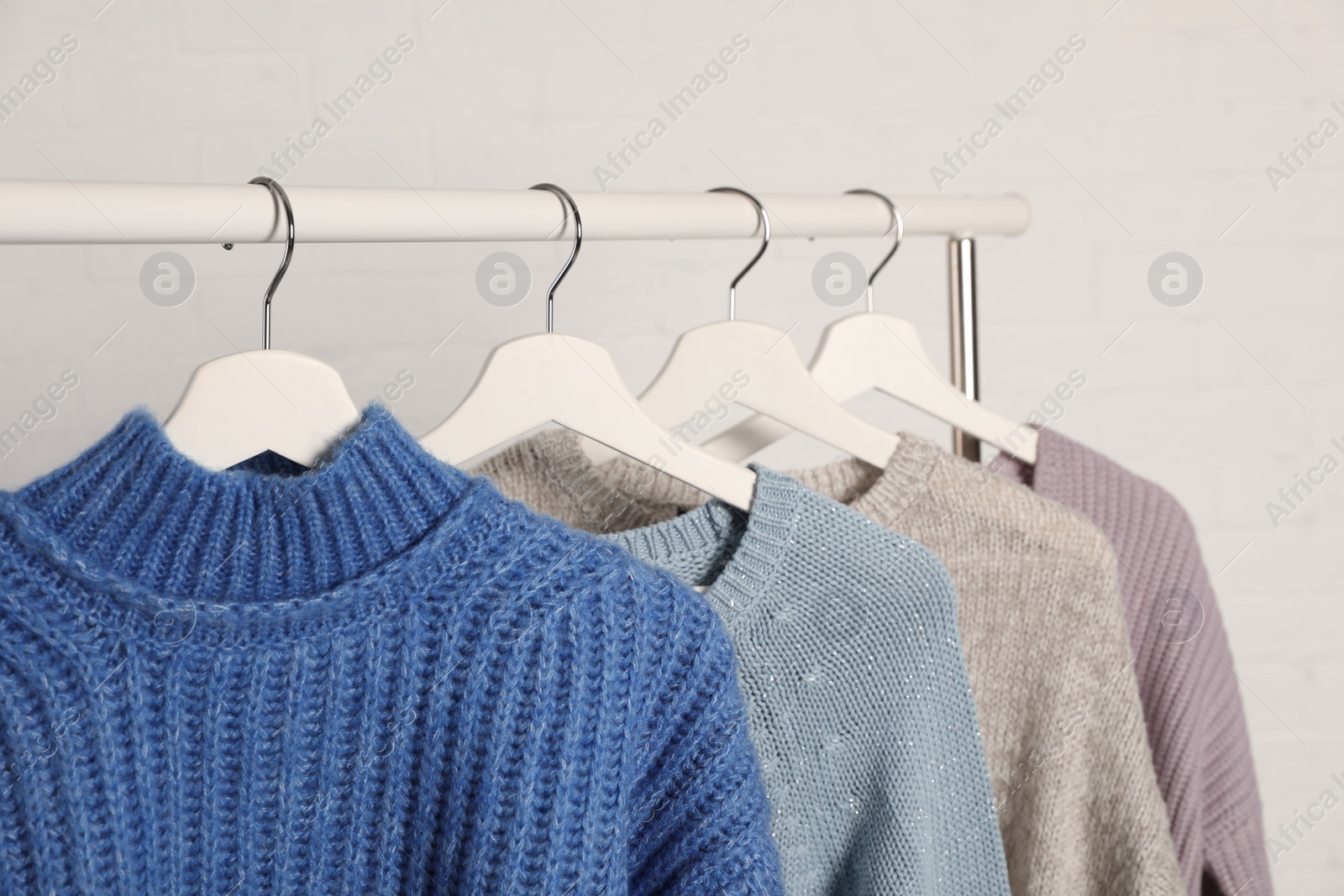 Photo of Collection of warm sweaters hanging on rack against white background, closeup