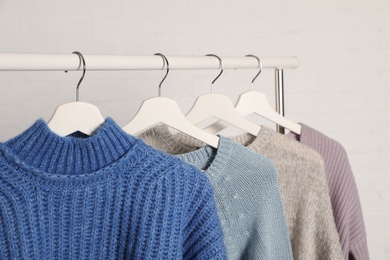 Photo of Collection of warm sweaters hanging on rack against white background, closeup