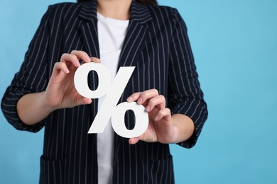 Photo of Woman holding percent sign on light blue background, closeup