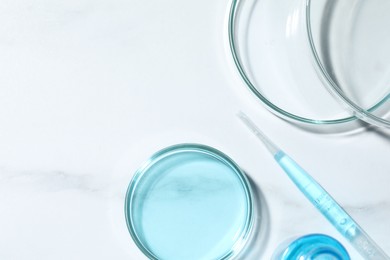 Pipette and petri dishes with liquid on white marble table, flat lay