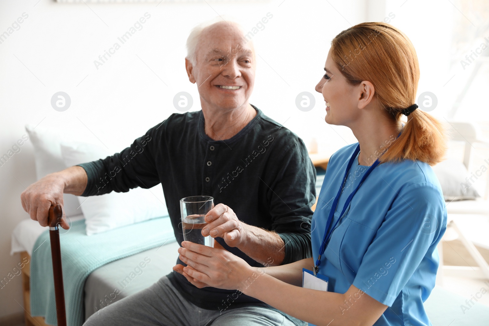 Photo of Nurse giving glass of water to elderly man indoors. Medical assistance