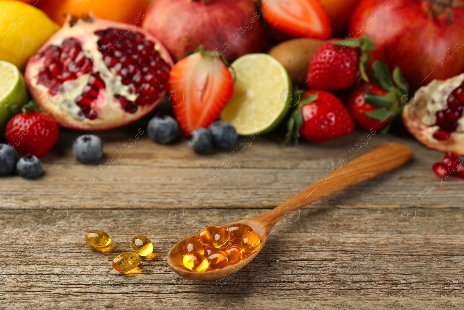 Photo of Vitamin pills in spoon and fresh fruits on wooden table