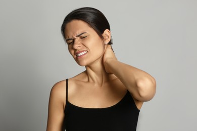 Photo of Young woman suffering from neck pain on grey background