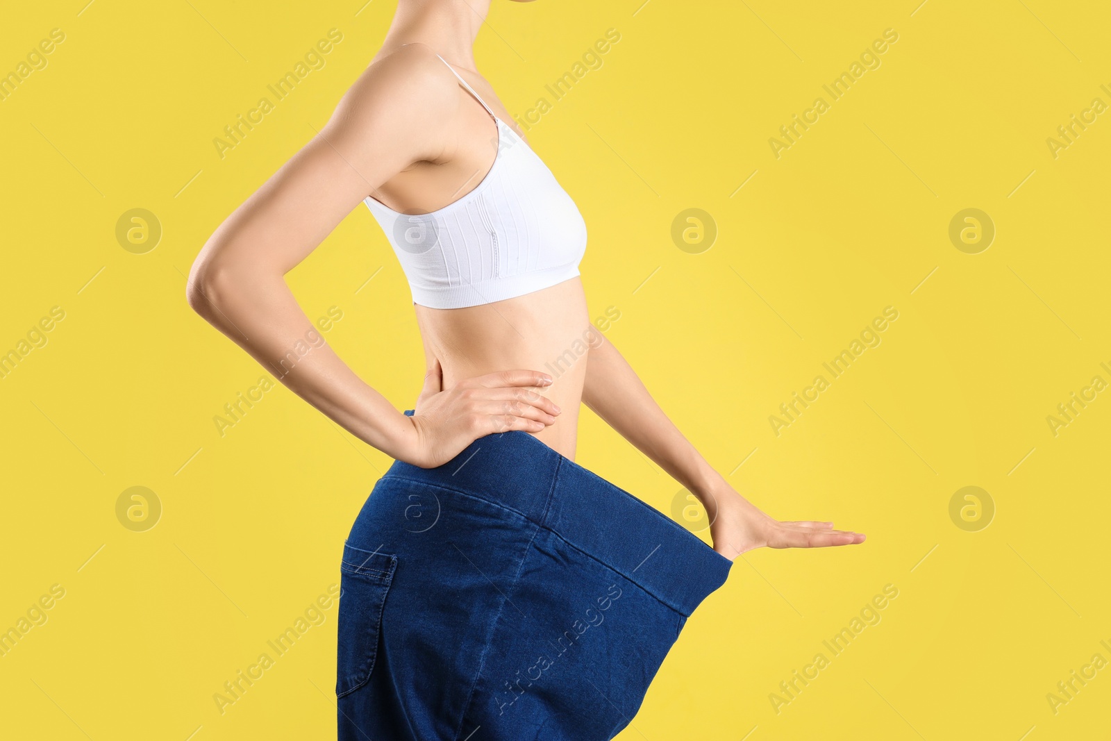 Photo of Young slim woman wearing oversized jeans on yellow background, closeup