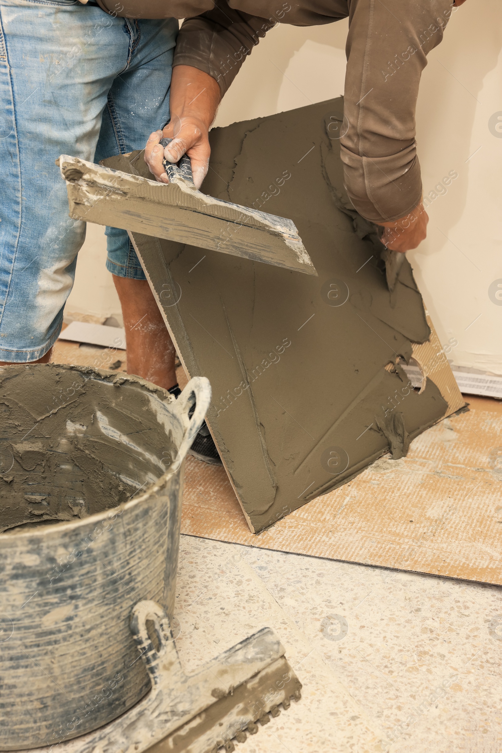 Photo of Worker spreading adhesive mix over tile with spatula, closeup