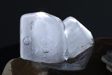Photo of Crystal clear ice cubes on stone against dark background, closeup