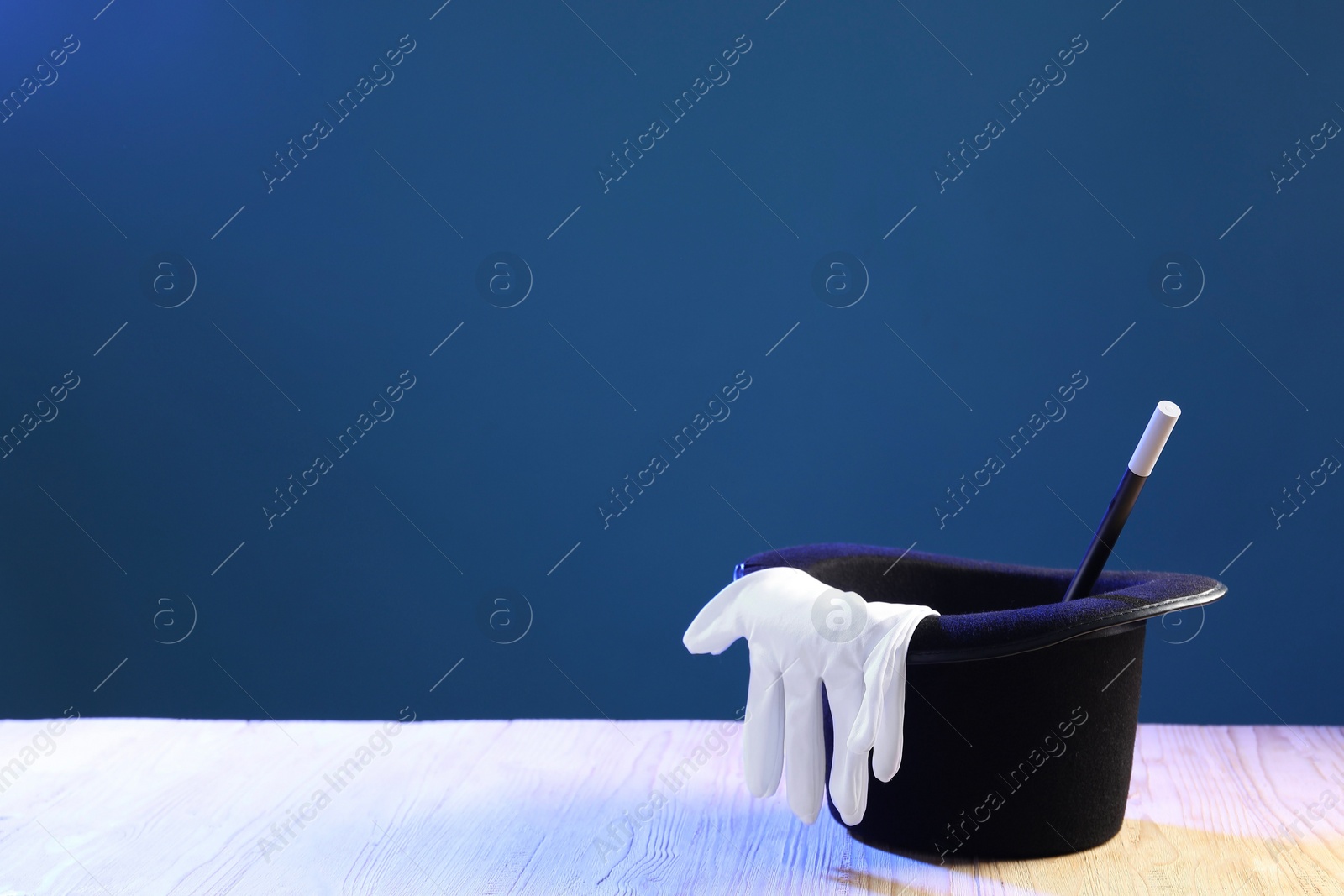 Photo of Magician's hat, wand and gloves on wooden table against blue background, space for text